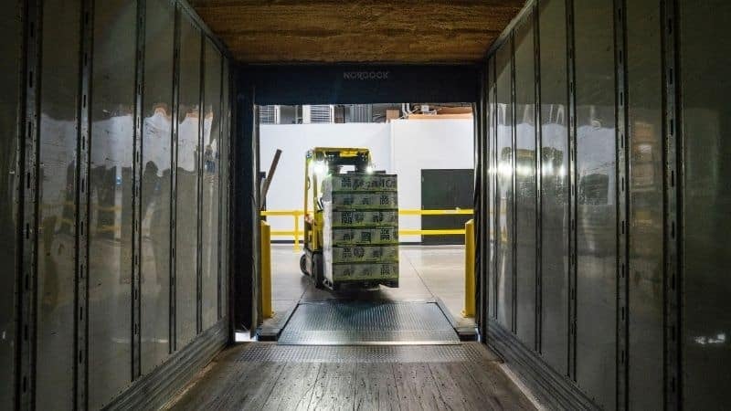 A manual forklift carrying a load of pallets into a shipping container