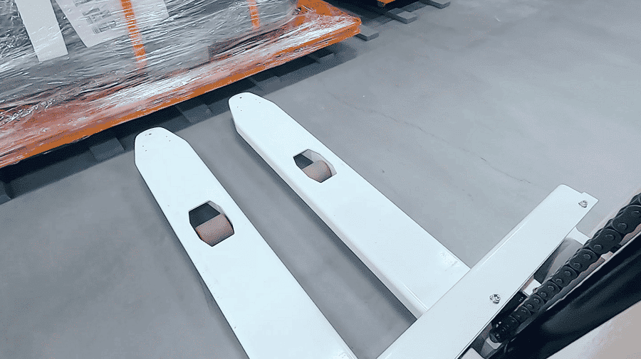 An automated vehicle's forks moving under a pallet.